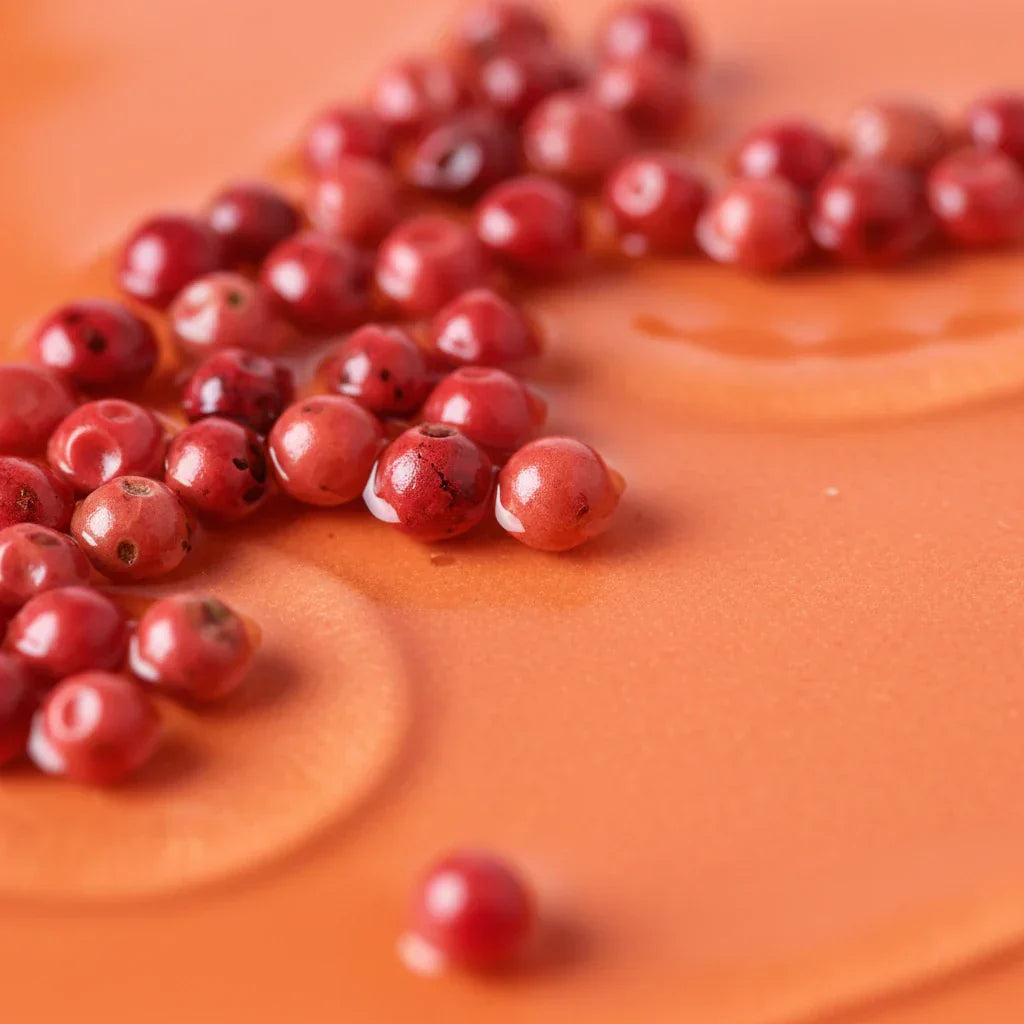Pink peppercorns scattered on a warm orange surface