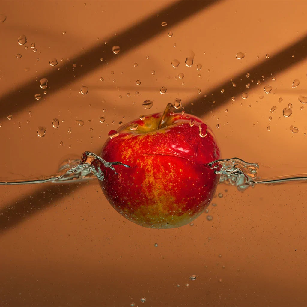 Red apple splashing into water against a warm orange background