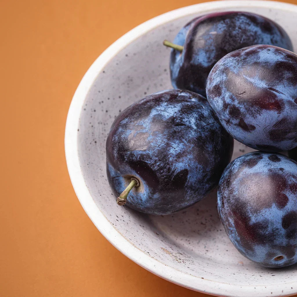 Fresh plums in a bowl on an orange background — plum fragrance note spotlight