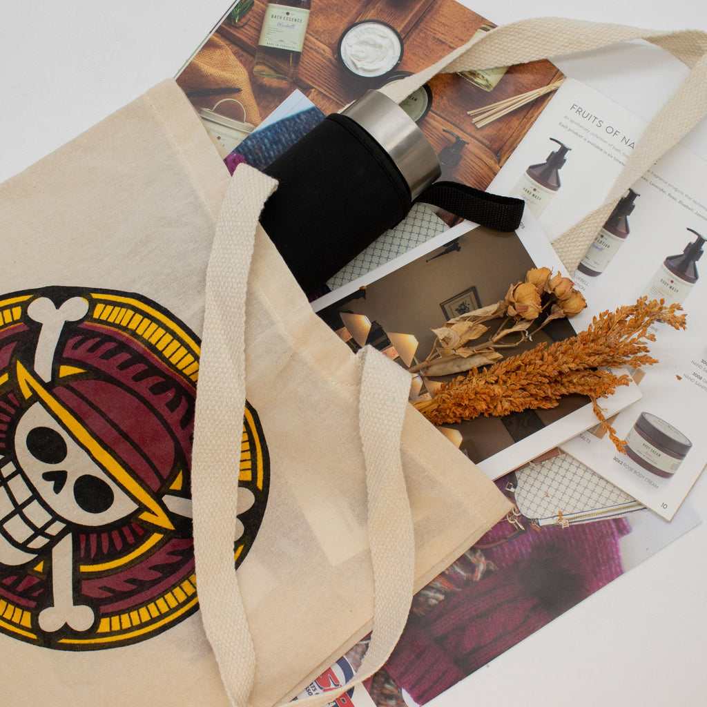 Beige tote bag with a colorful design on a surface with books and a small plant.