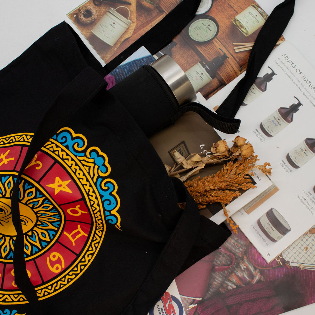 Black tote bag with colorful zodiac design on a magazine background