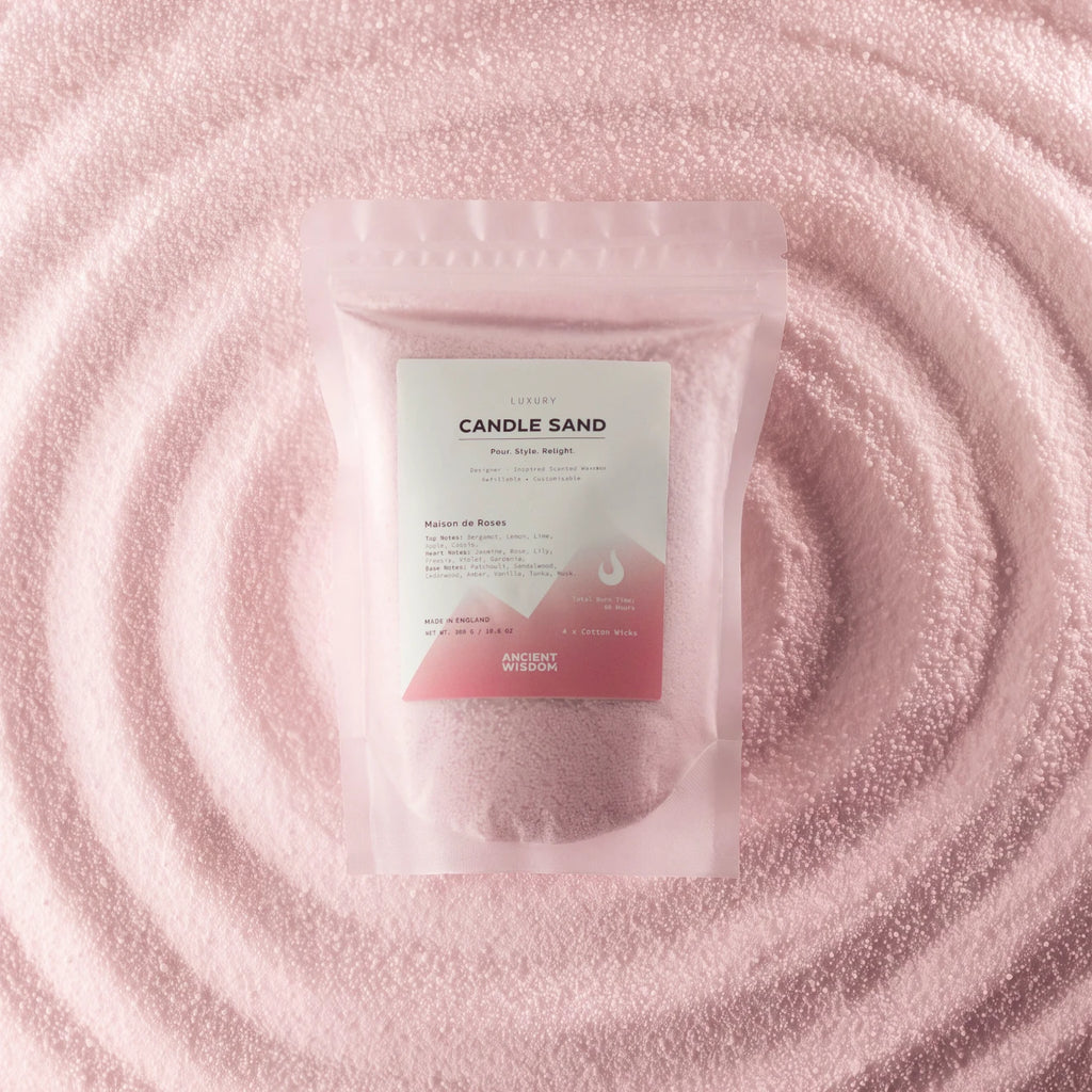 A stand-up pouch labeled 'CANDLE SAND' with a white and pink label, placed on a textured pink surface with concentric circular ripples behind it.