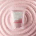 A stand-up pouch labeled 'CANDLE SAND' with a white and pink label, placed on a textured pink surface with concentric circular ripples behind it.