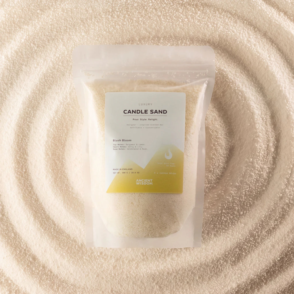 A stand-up pouch labeled 'CANDLE SAND' containing pale cream wax, placed on a textured surface of matching cream wax in a circular pattern. The label has a white top half and a yellow-green geometric bottom section.