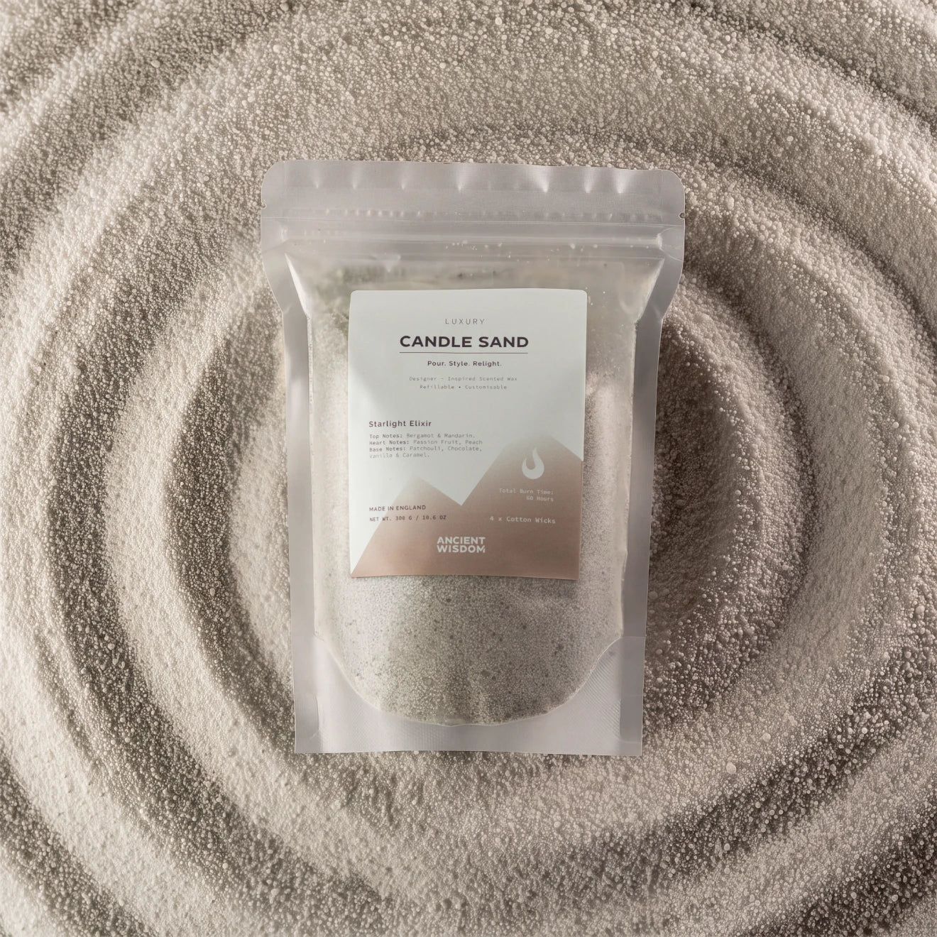 A clear stand-up pouch labeled 'Candle Sand' containing a light beige textured powder, placed on top of concentric rings of the same powder. The pouch has a white and taupe label with the brand name Ancient Wisdom visible near the bottom.