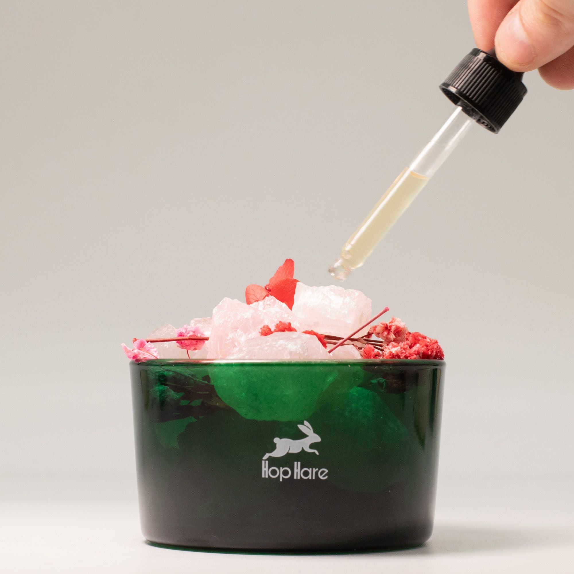 Hop Hare Diffusing Crystals & Floral Set to add liquid to a Green container with ice and red flowers, dropper adding liquid, brand 'flop hare' visible