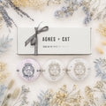 Three bath bombs with 'Agnes + Cat' branding on a decorative background with flowers and a gift box.