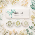 Three bath pillows with 'Agnes + Cat' branding on a white background with decorative plants.