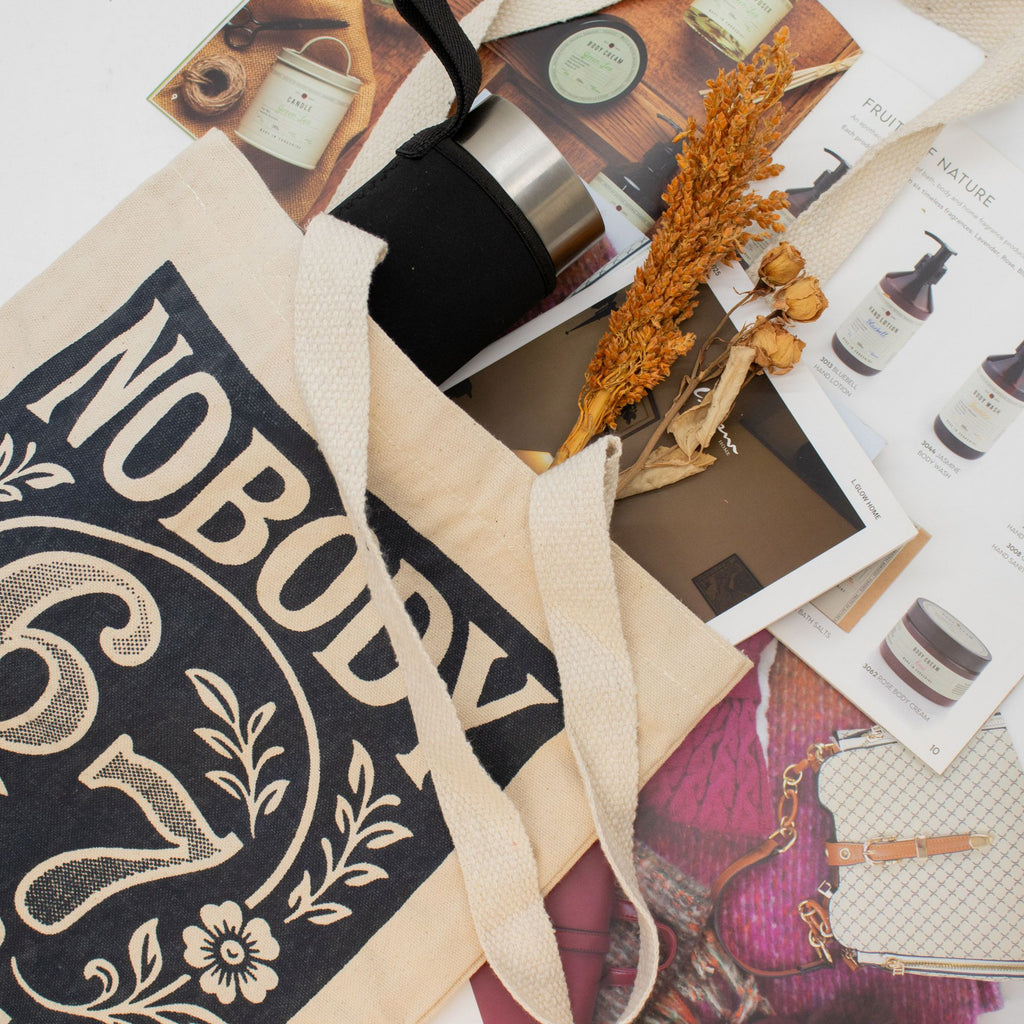 Tote bag with 'NOBODY knows 6 7' text on a surface with various items including a candle and magazine.