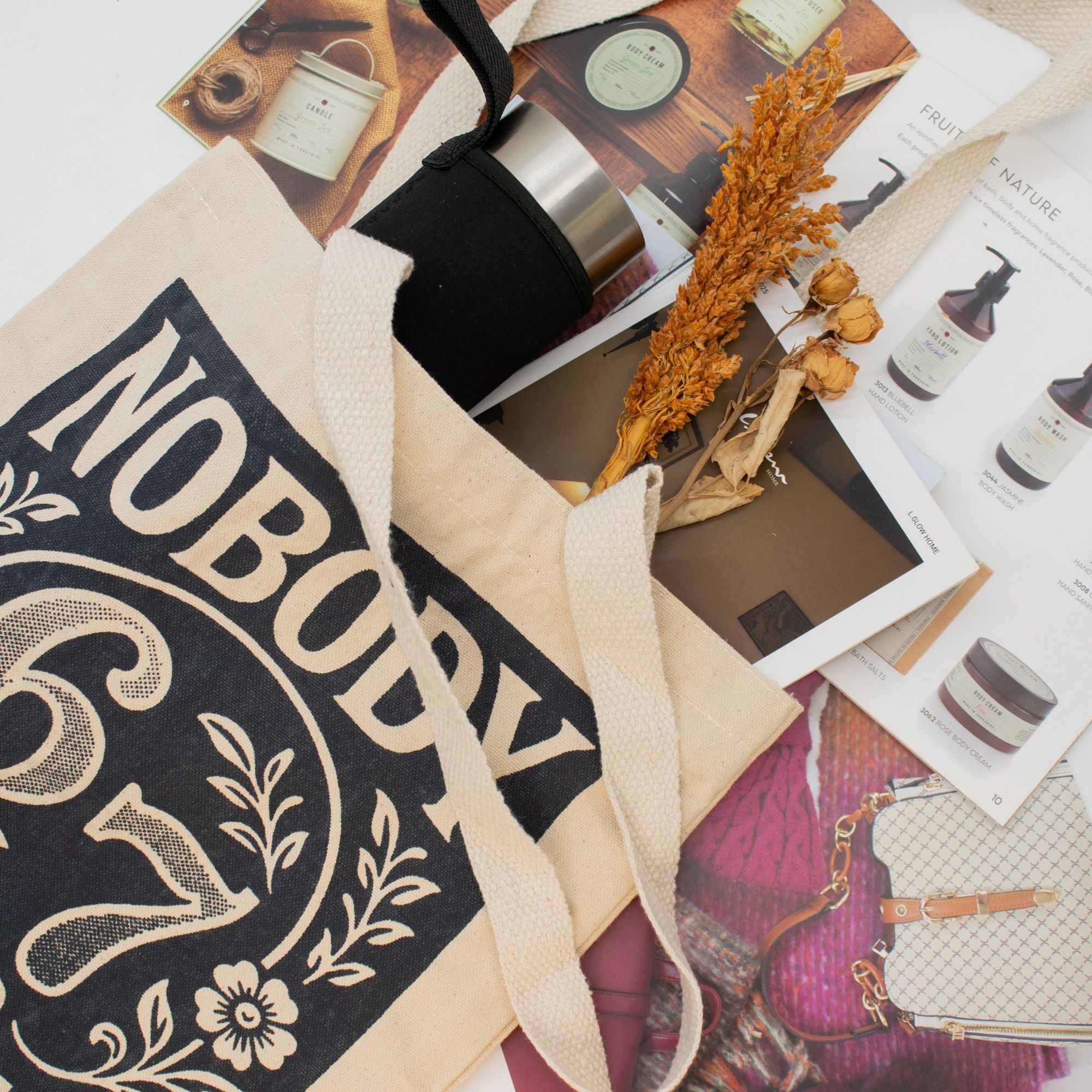 Tote bag with 'NOBODY knows 6 7' text on a surface with various items including a candle and magazine.