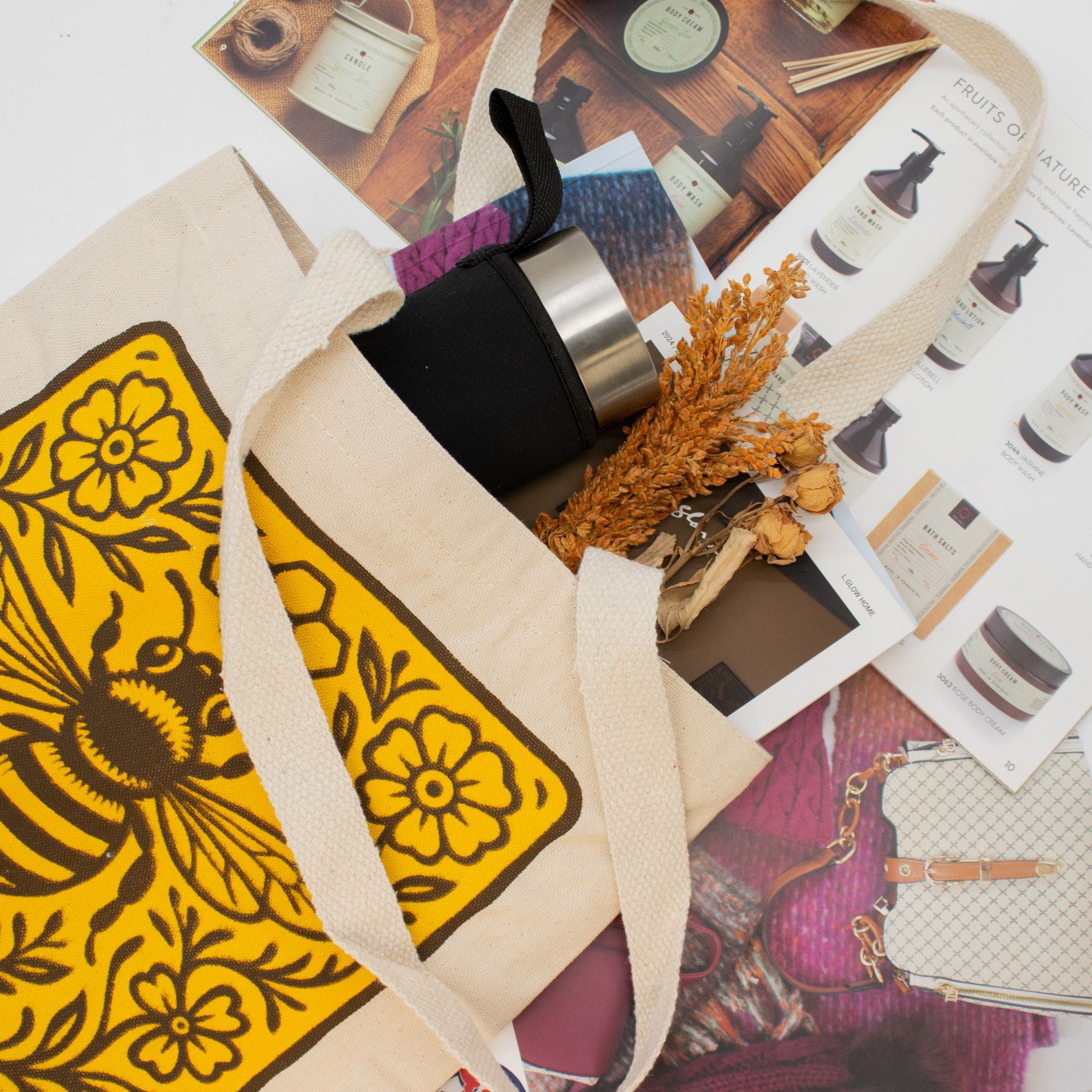 Tote bag with yellow floral patterns containing a black and gold bottle, on a surface with various items.